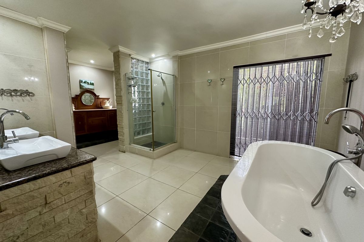 Spacious bathroom featuring a freestanding bathtub, glass-enclosed shower with glass block accents, double vanity with stone cladding, and large format floor tiles.