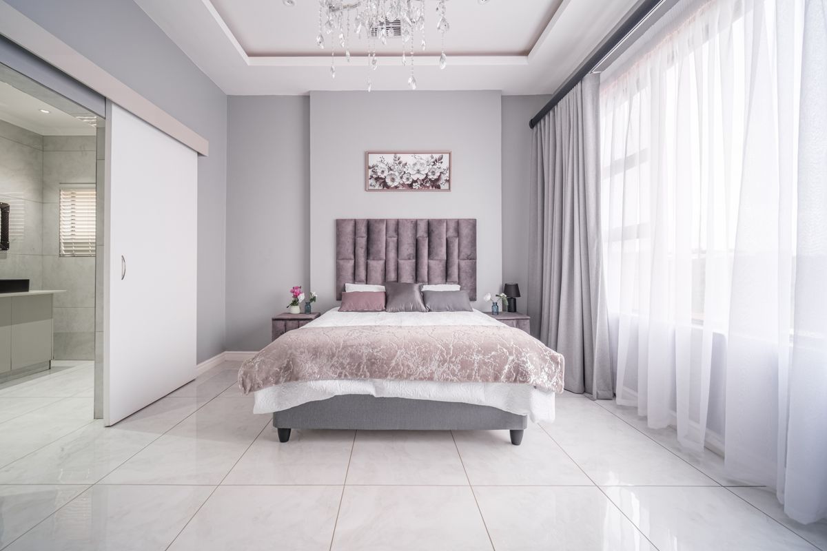 Spacious bedroom featuring large format floor tiles, a recessed tray ceiling with integrated lighting, and an adjoining en-suite bathroom with sliding door access.