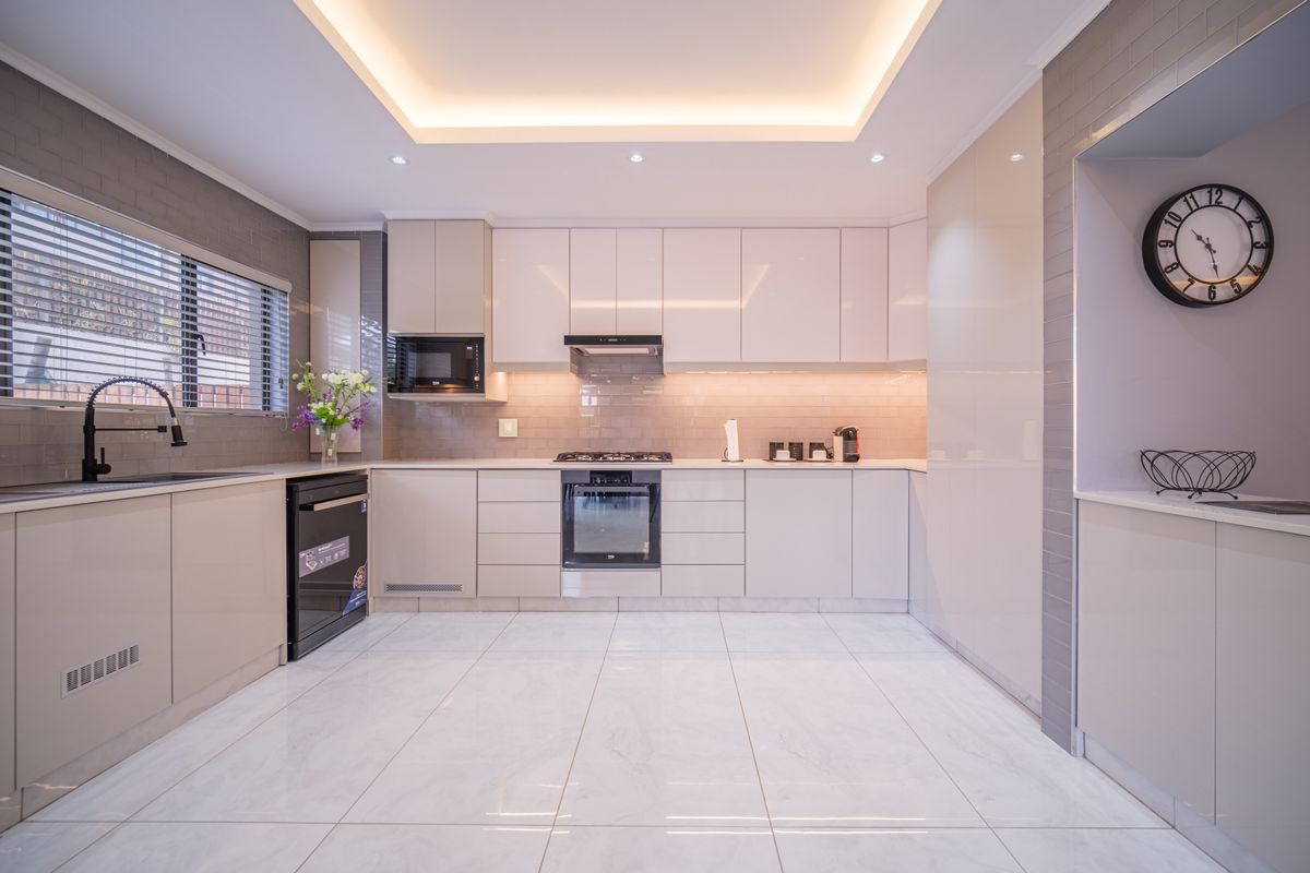 Modern kitchen featuring high-gloss cabinetry, integrated oven, gas hob, extractor fan, stone countertops, and recessed tray ceiling lighting.