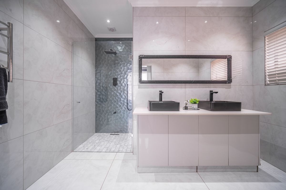 Modern bathroom featuring a double vanity with black vessel sinks, a walk-in glass shower with textured feature tiling, and large-format wall tiles.