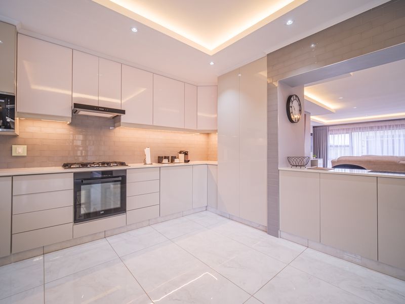 Modern open-plan kitchen featuring high-gloss cabinetry, integrated oven, gas hob, extractor fan, and sleek tiled flooring with recessed ceiling lighting.