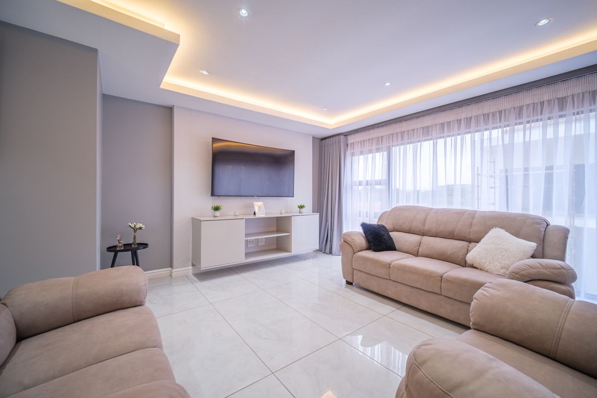 Modern living room featuring polished porcelain floor tiles, recessed ceiling lighting with cove detail, and a wall-mounted media console.