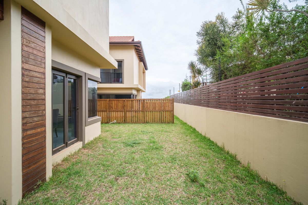 A private rear garden area featuring a manicured lawn, perimeter boundary walls, and timber slat fencing, providing a secure outdoor space.