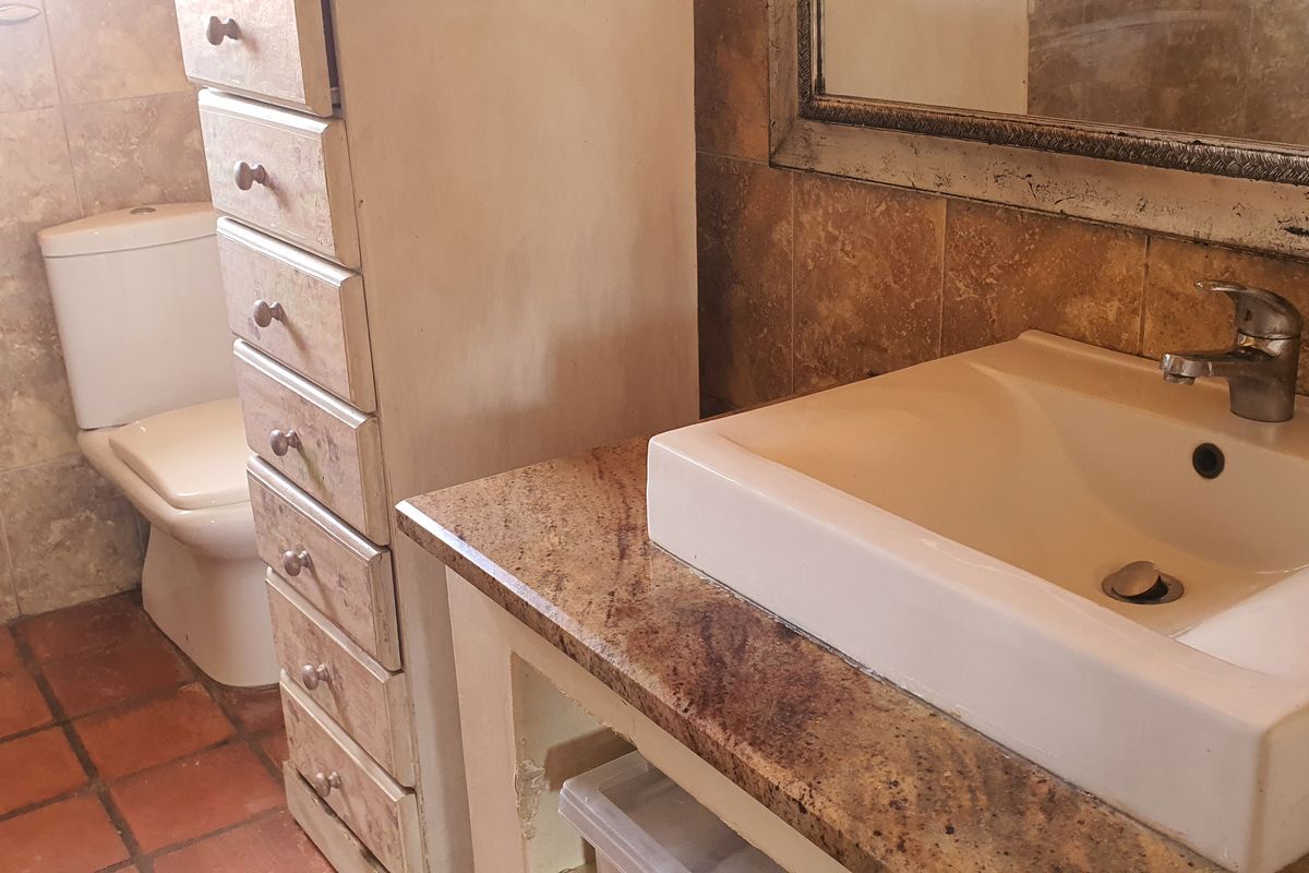 A functional bathroom featuring a granite-topped vanity with a ceramic basin, tiled walls, and a standard toilet.