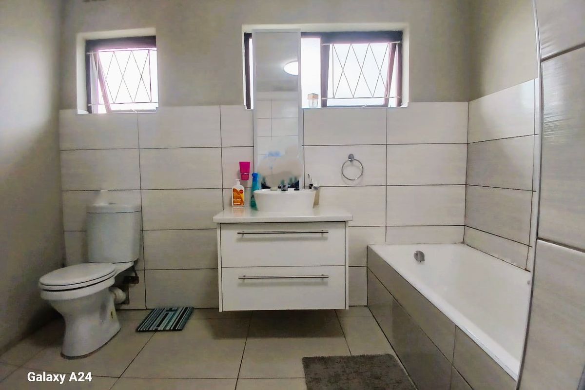 A functional bathroom featuring a modern vanity with vessel sink, a standard toilet, and a bathtub with neutral wall and floor tiling.