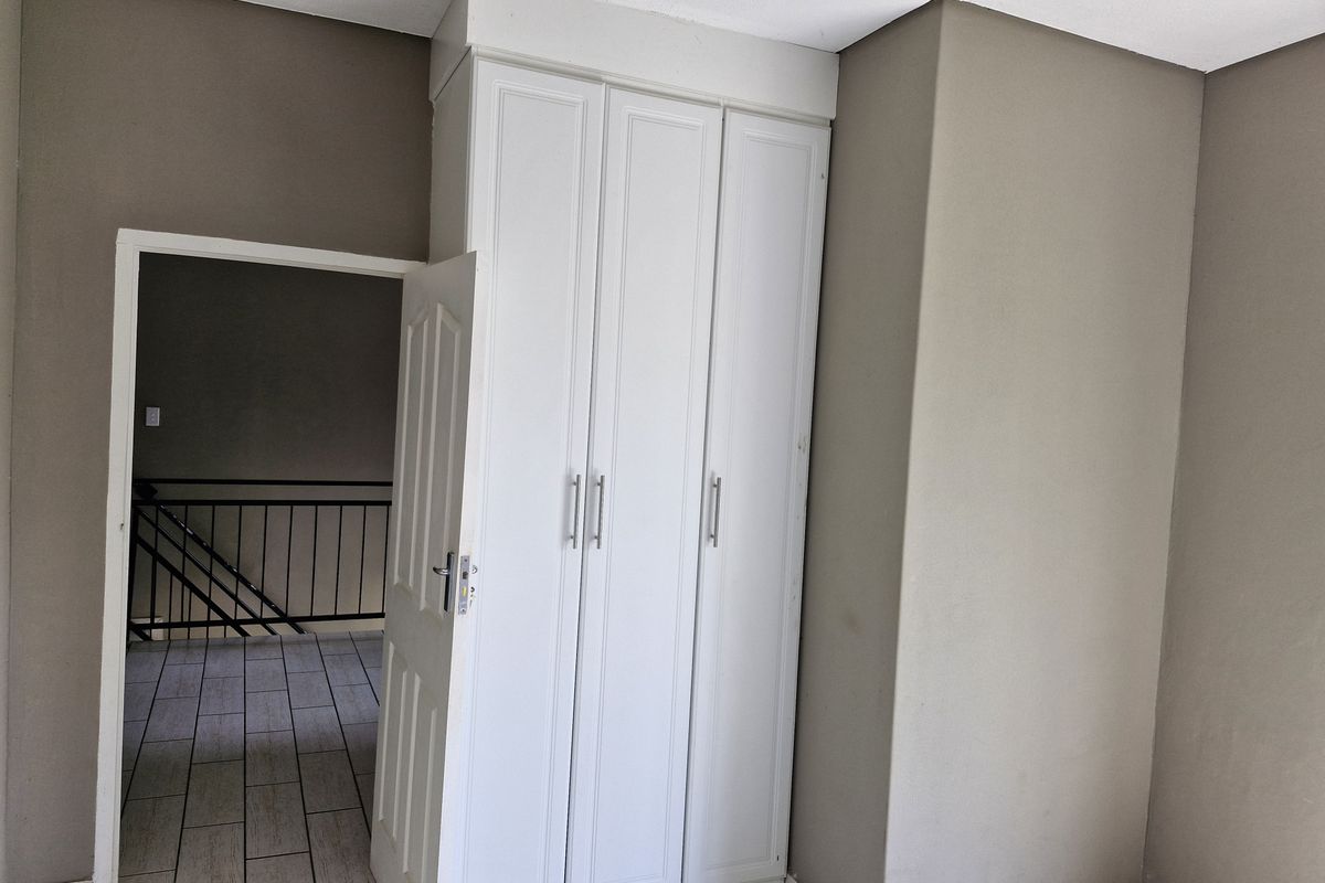A bedroom featuring built-in white cabinetry and tiled flooring, with an open doorway leading to a hallway with a staircase.