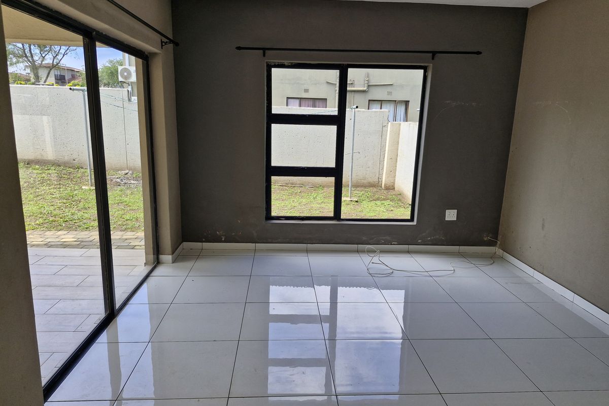 An empty living room featuring large format floor tiles, dark grey accent walls, and sliding glass doors providing direct access to the rear patio.