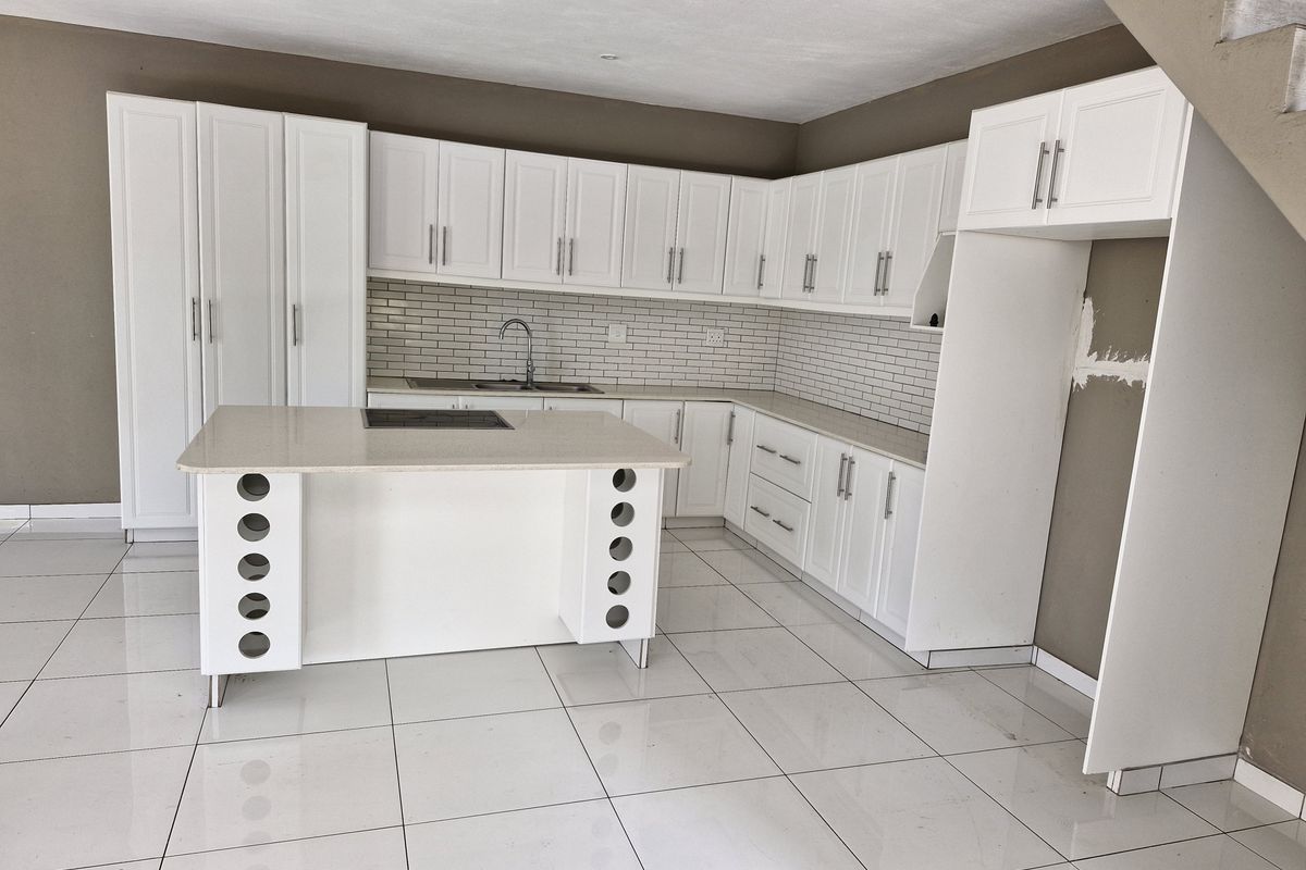 Modern kitchen featuring white cabinetry, stone countertops, a central island with integrated hob, and subway tile backsplash, set against a neutral wall finish.