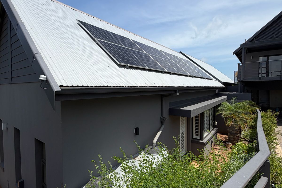 Rear exterior view of the property featuring a modern corrugated metal roof with integrated solar panels and a rainwater collection tank.