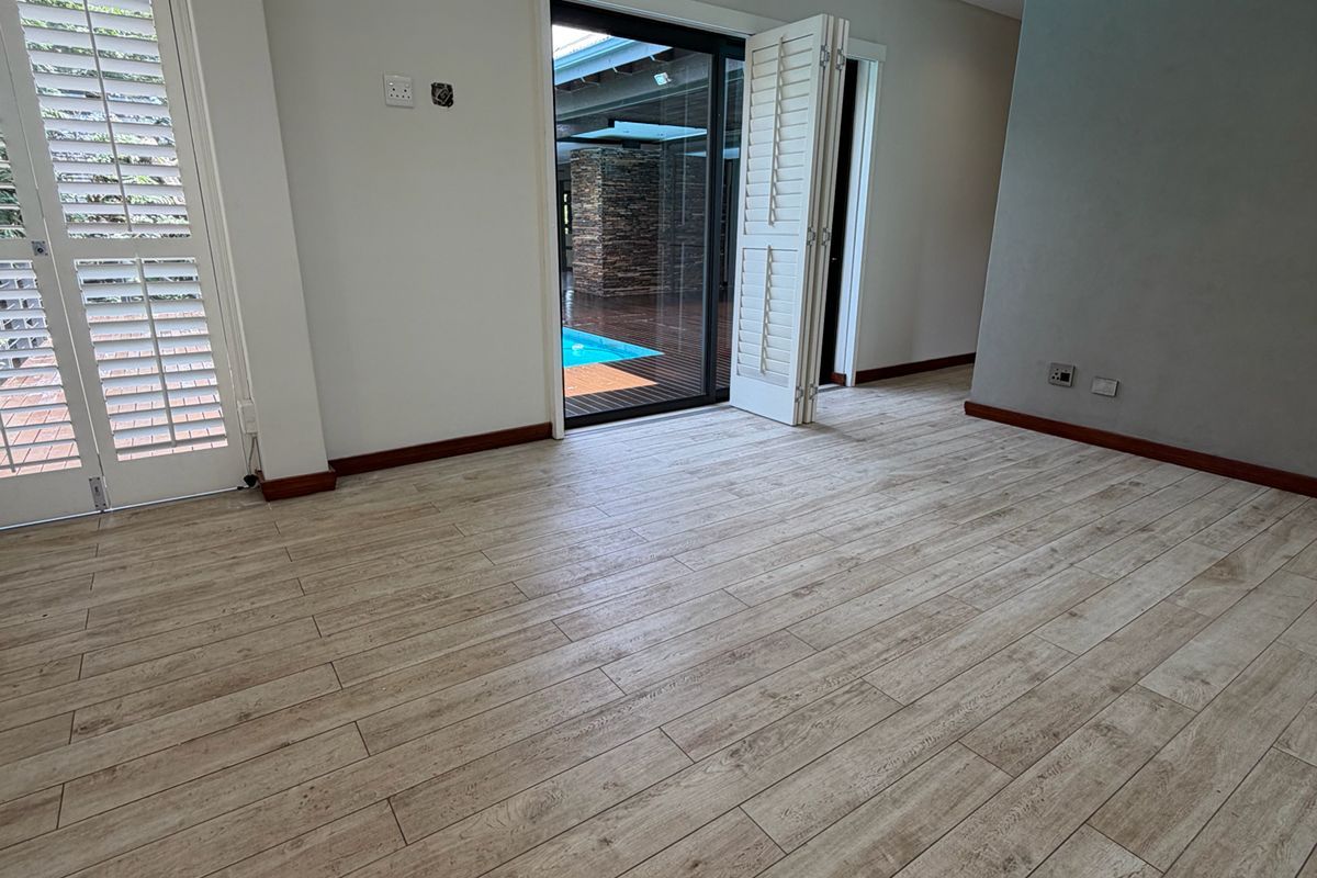 Spacious living area featuring wood-look tile flooring, recessed lighting, and plantation shutters, with direct access to an outdoor patio and pool area.