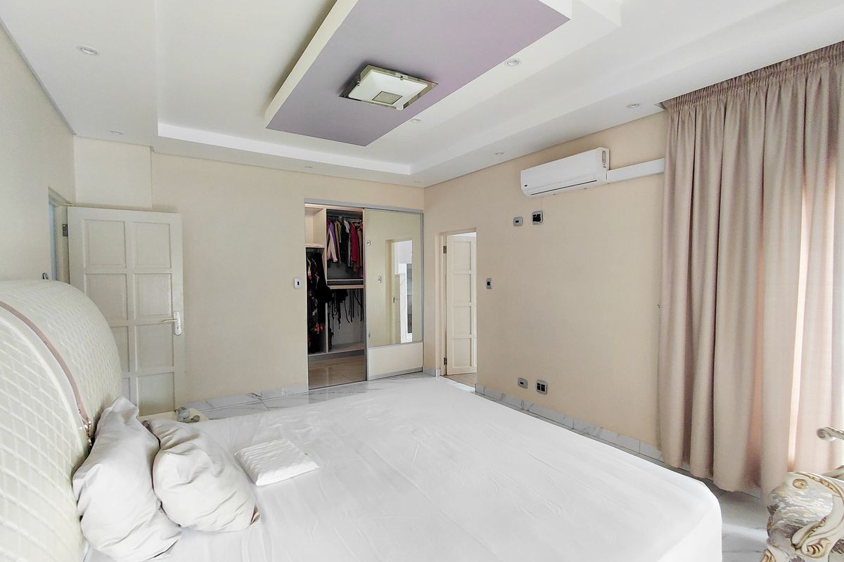 Spacious bedroom featuring a recessed ceiling with accent lighting, built-in closet with mirrored doors, and wall-mounted air conditioning unit.