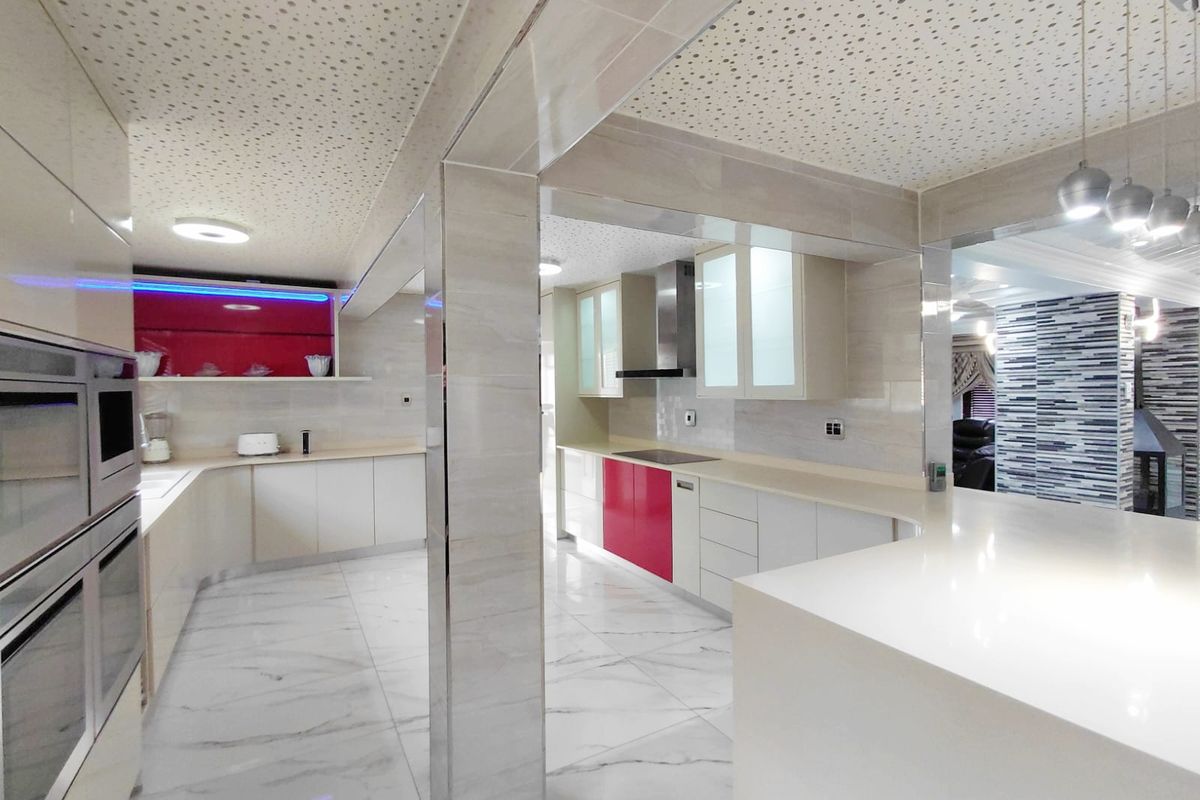 Modern kitchen featuring high-gloss cabinetry, stone countertops, integrated stainless steel appliances, and marble-look floor tiles with a unique perforated ceiling design.