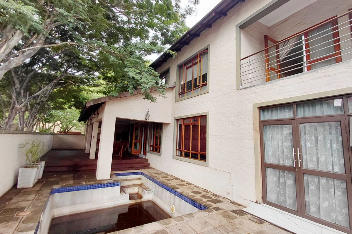 Rear exterior view of a two-story house featuring a swimming pool, covered patio area, and a second-floor balcony with metal railings.