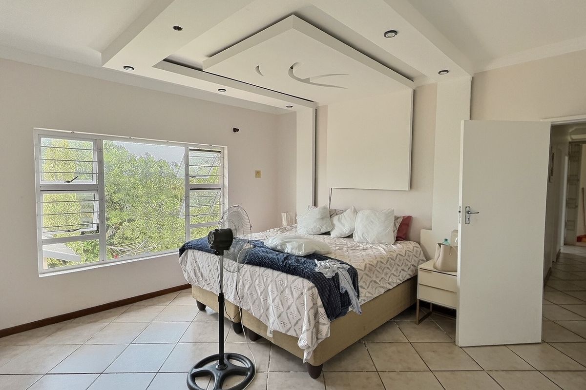 A spacious bedroom featuring a decorative recessed ceiling with integrated downlights, large windows, and tiled flooring.