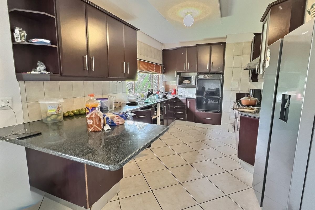 A functional kitchen featuring dark wood cabinetry, granite countertops, tiled flooring, and built-in oven and microwave units.