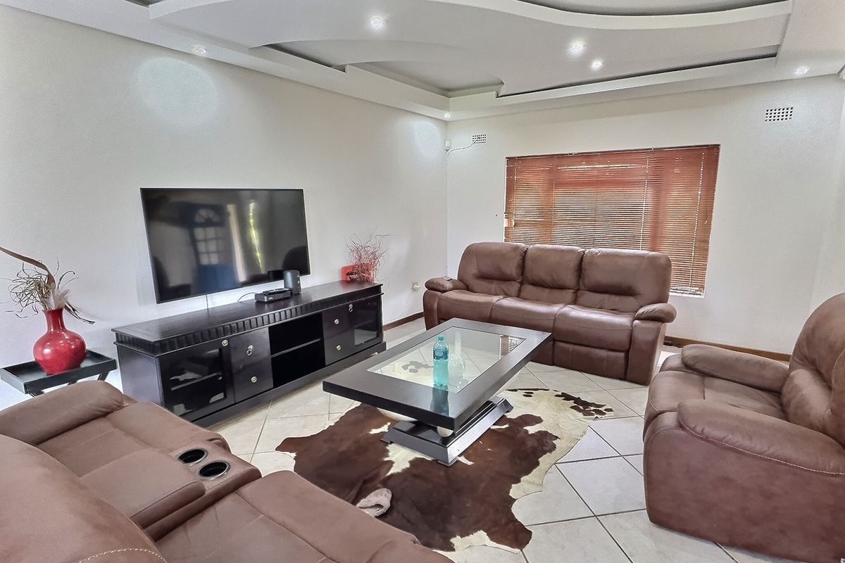 Spacious living room featuring a decorative recessed tray ceiling with integrated downlighting and neutral ceramic floor tiles.