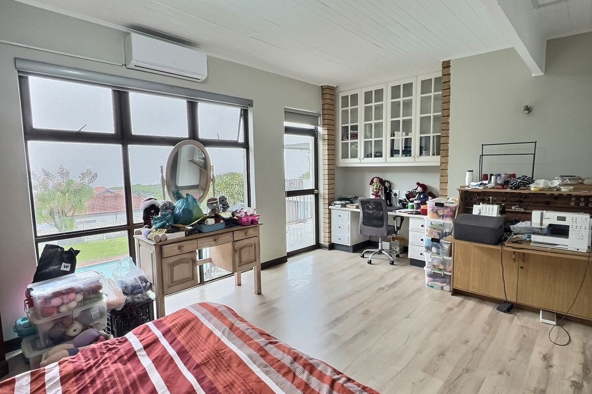 Spacious bedroom featuring light wood-look flooring, built-in cabinetry, a wall-mounted air conditioning unit, and large windows providing natural light and exterior views.