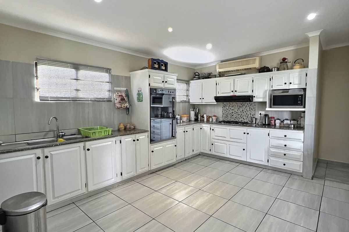 A functional kitchen featuring white cabinetry, built-in oven, hob, extractor fan, and tiled flooring with ample counter space.