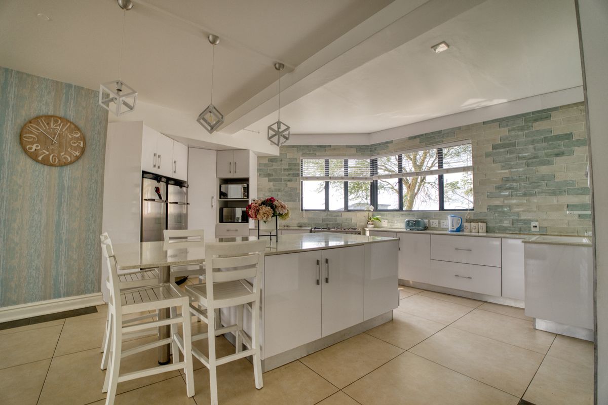 Modern kitchen featuring a central island with quartz countertops, sleek white cabinetry, a decorative subway tile backsplash, and ample natural light.