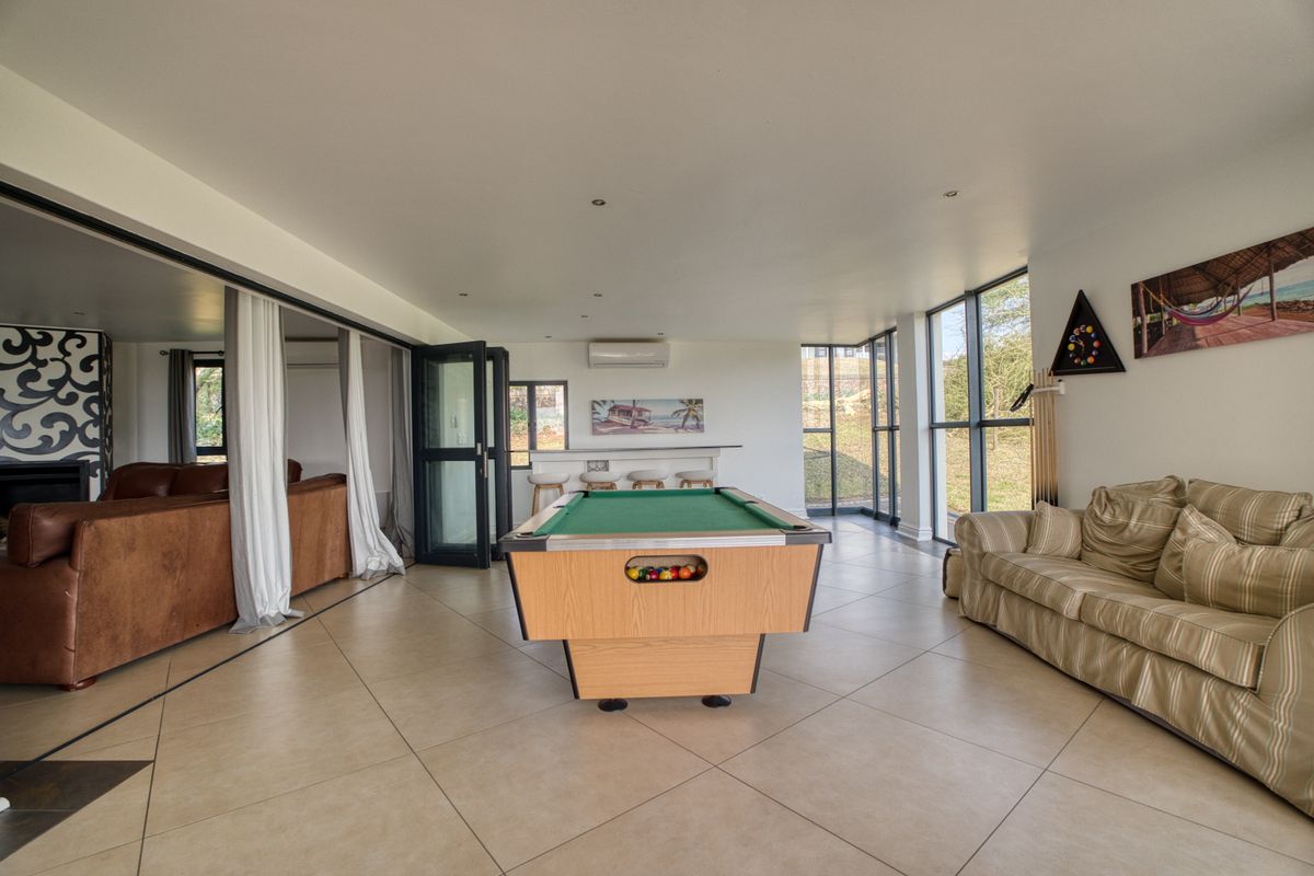 Spacious living area featuring large glass sliding doors, floor-to-ceiling windows, tiled flooring, and a built-in bar counter, offering a bright and open entertainment space.