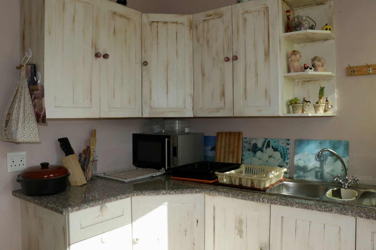 A compact kitchen corner featuring distressed white cabinetry, granite-look laminate countertops, and a stainless steel sink with a mixer tap.