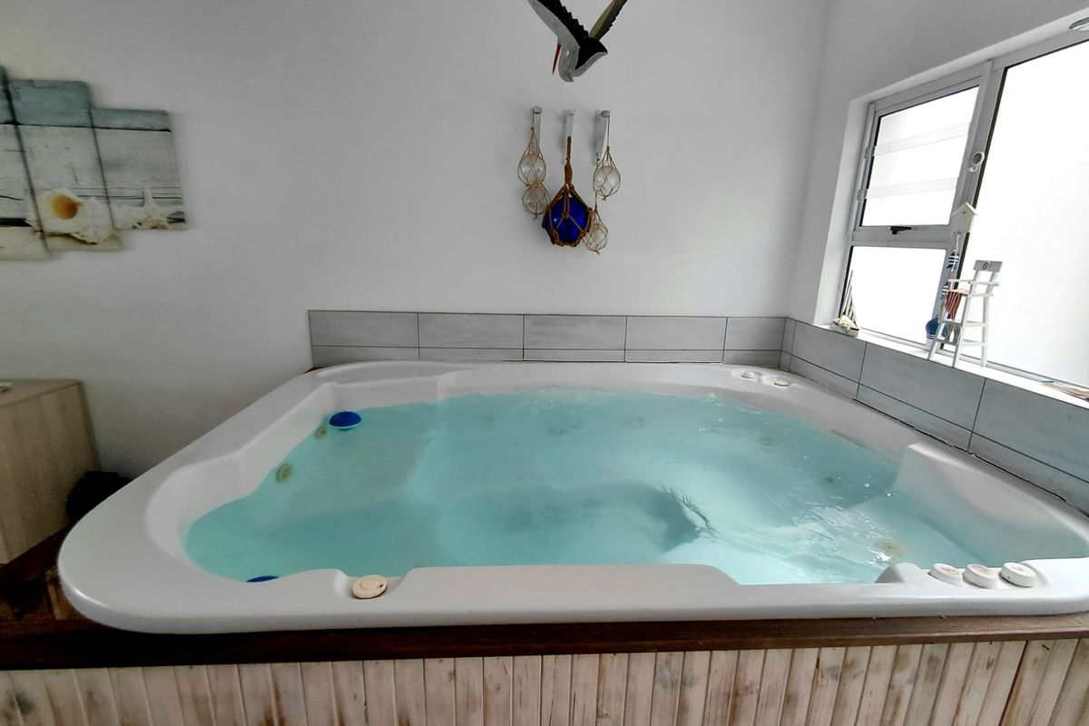 A built-in indoor spa bath featuring tiled splashbacks and a rustic timber-paneled surround, positioned beneath a window.