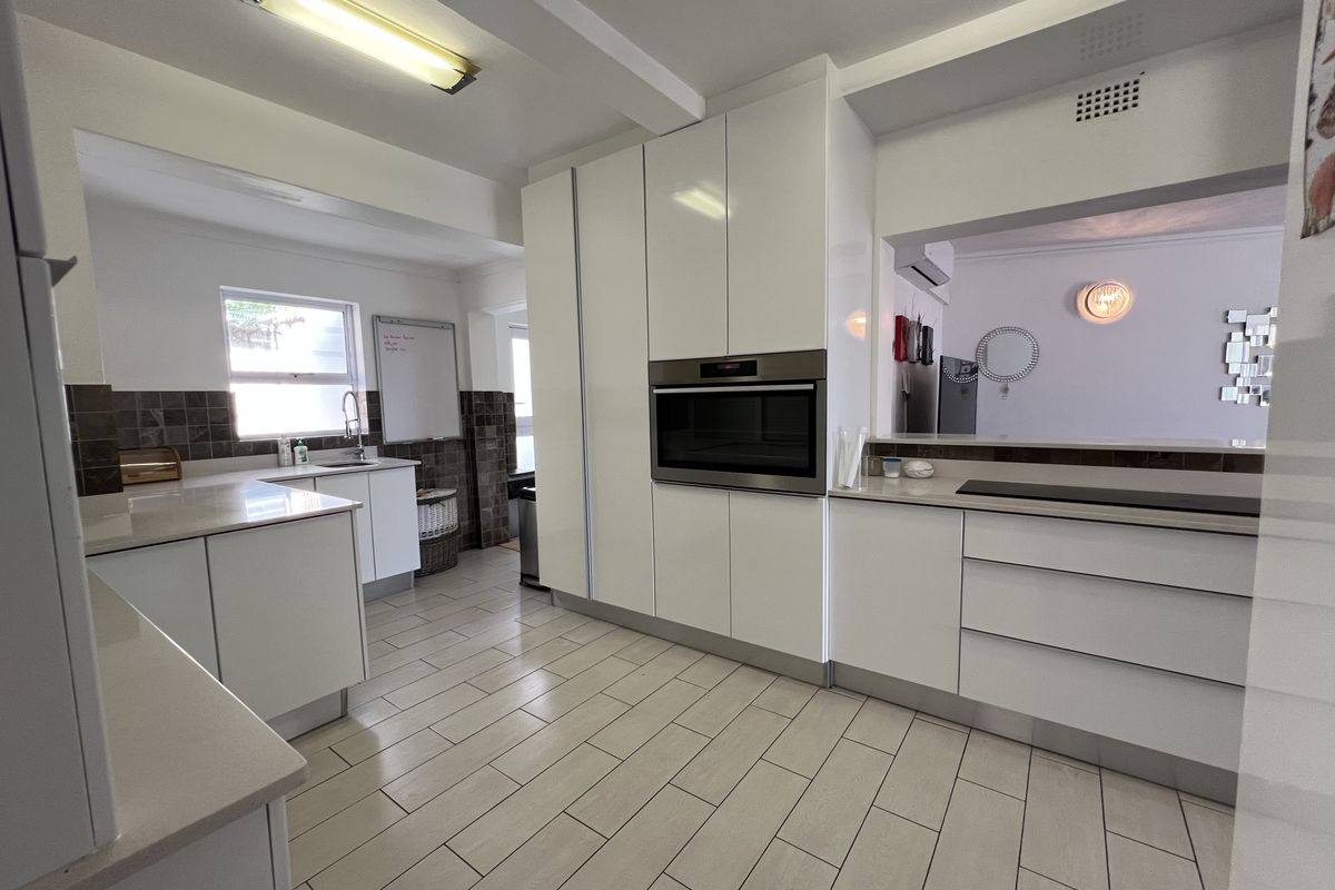 Modern kitchen featuring white cabinetry, stone countertops, built-in oven, and tiled flooring with a convenient pass-through window to the living area.