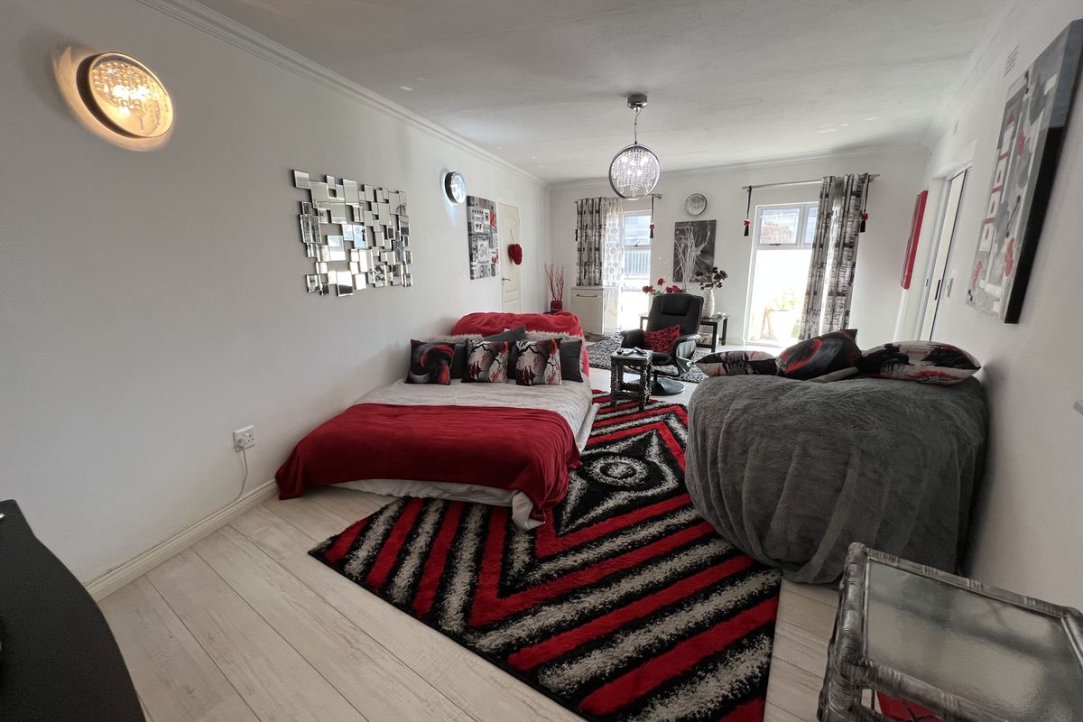 A spacious bedroom featuring light-toned wood-look flooring, built-in sliding door wardrobes, and direct access to an outdoor area through glass doors.