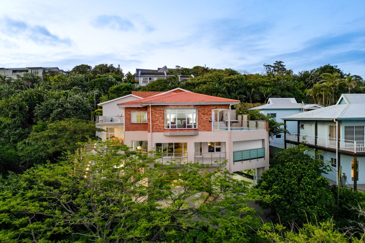 Aerial view of a multi-story residential property featuring a terracotta tile roof, brick and rendered facade, and multiple balconies nestled in a lush environment.