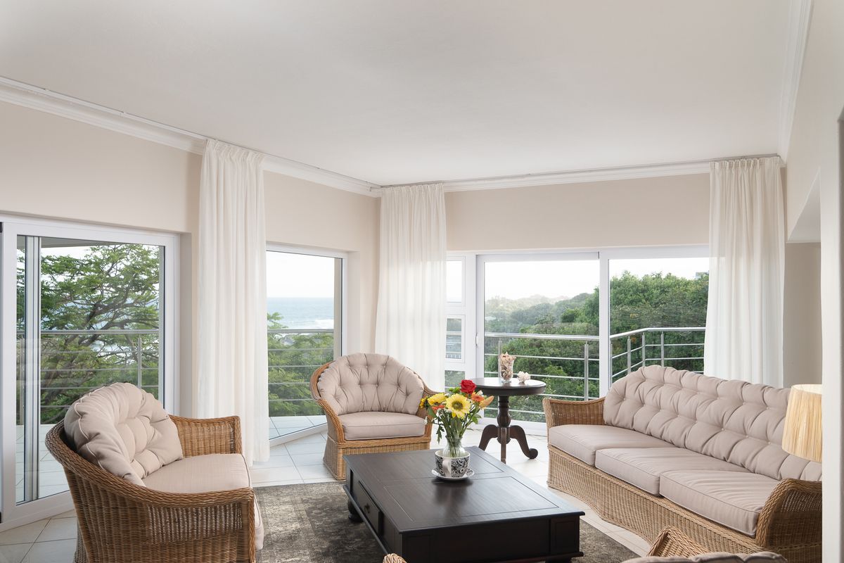Bright living room featuring large sliding glass doors that open to a balcony with scenic coastal views and neutral tiled flooring.
