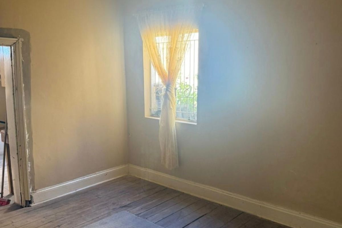 A vacant bedroom featuring original timber flooring, a window with security bars, and an unfinished doorway, offering a blank canvas for renovation.