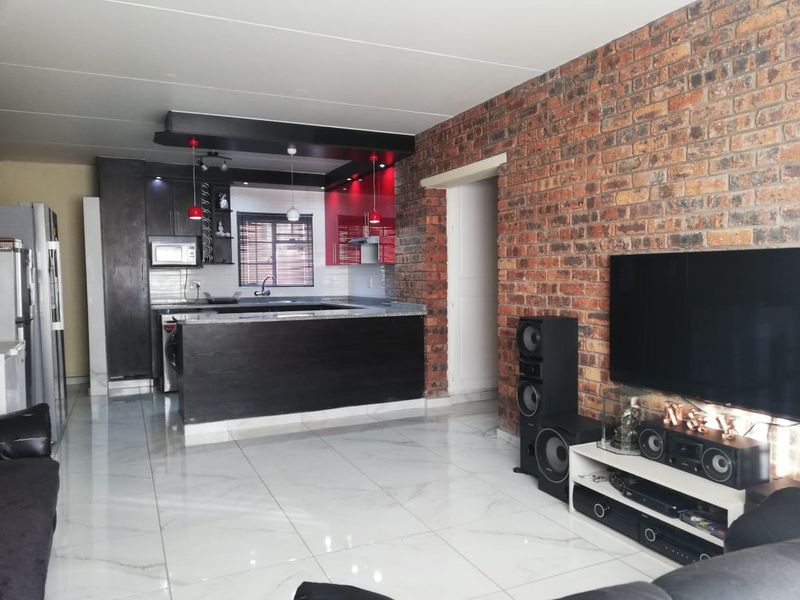 Open-plan living area featuring a modern kitchen with dark cabinetry, granite countertops, and a striking exposed brick feature wall with polished porcelain flooring.