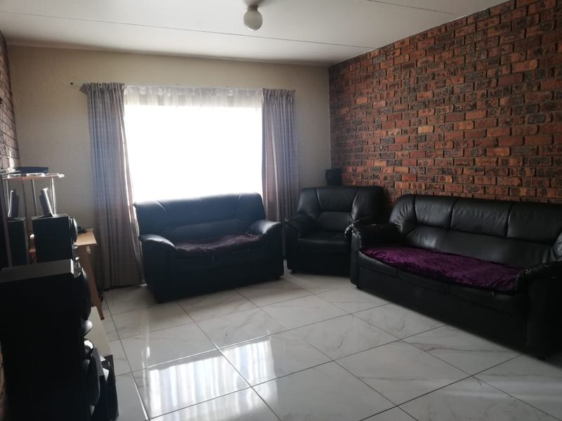 A living room featuring a prominent exposed brick feature wall and modern white porcelain floor tiles, providing a neutral base for interior design.