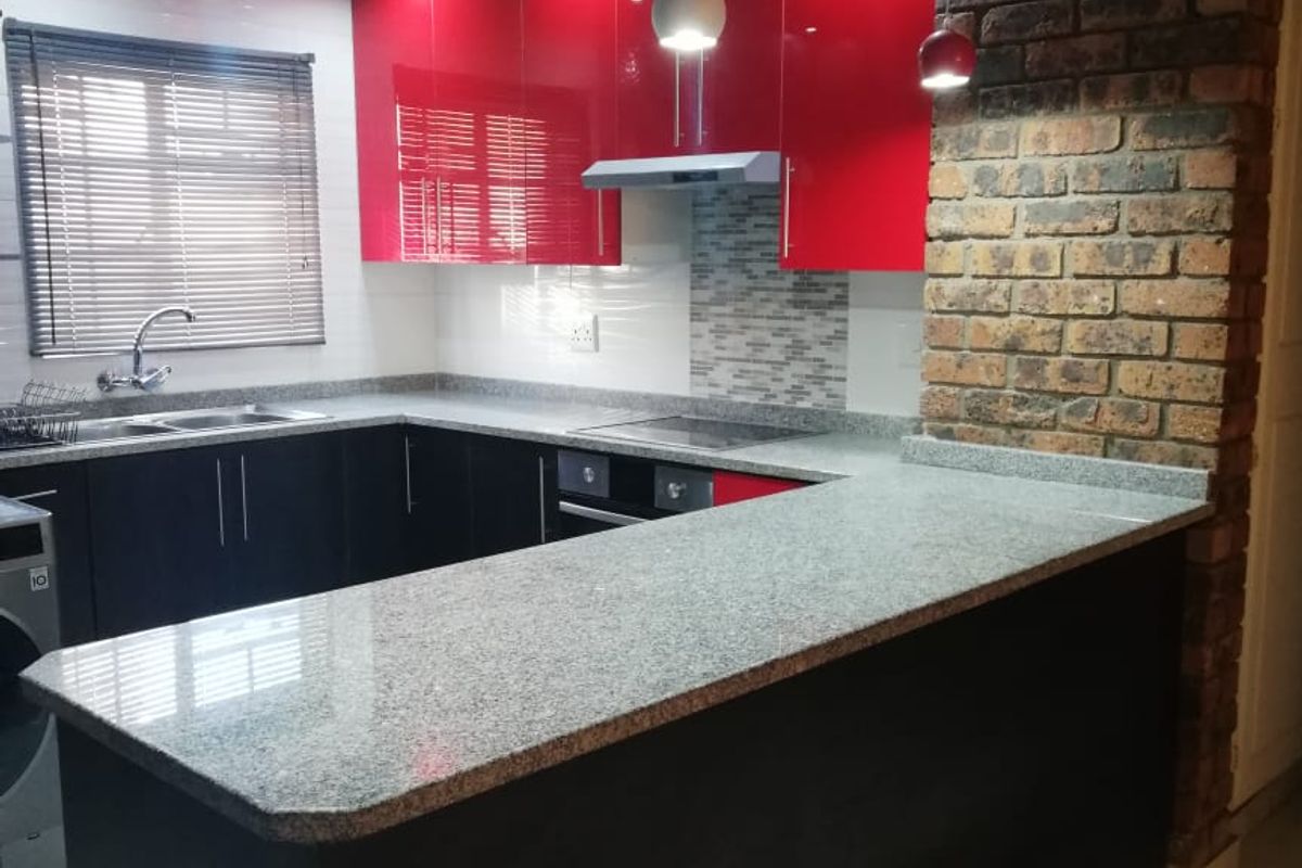 Modern kitchen featuring high-gloss red and black cabinetry, granite countertops, an exposed brick feature wall, and integrated appliances.