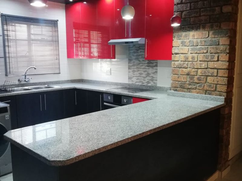 Modern kitchen featuring high-gloss red and black cabinetry, granite countertops, an exposed brick feature wall, and integrated appliances.