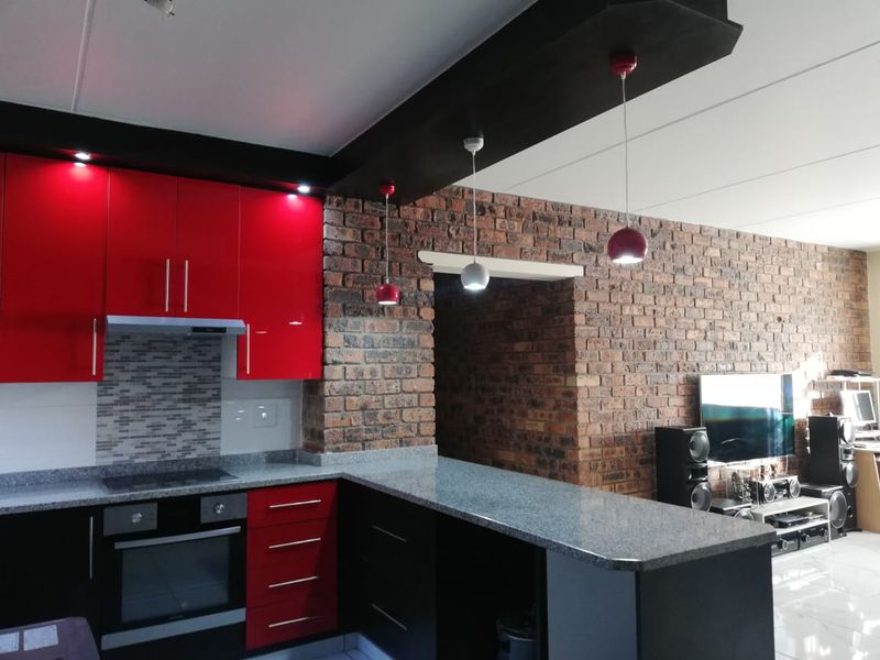 Modern open-plan kitchen featuring high-gloss red cabinetry, granite countertops, and a striking exposed brick feature wall with integrated lighting.