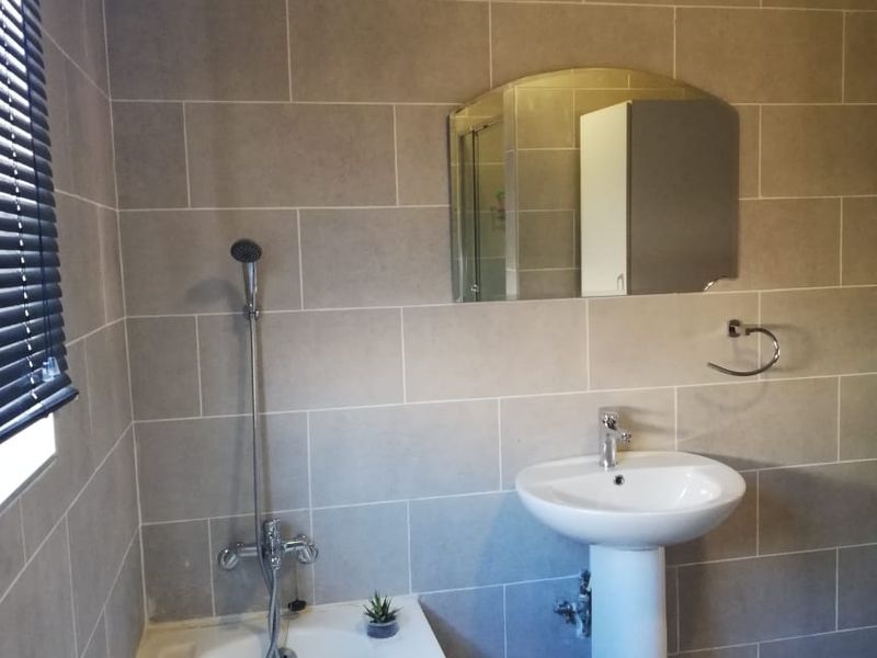 A clean, functional bathroom featuring a pedestal basin, bathtub with handheld shower mixer, and neutral wall tiling.