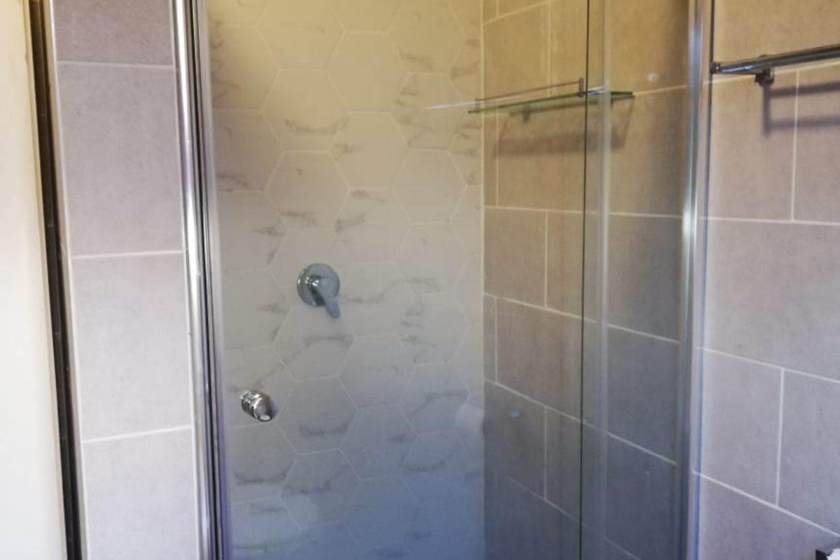 A clean, modern bathroom shower featuring a glass enclosure, chrome fixtures, and neutral-toned wall tiling.