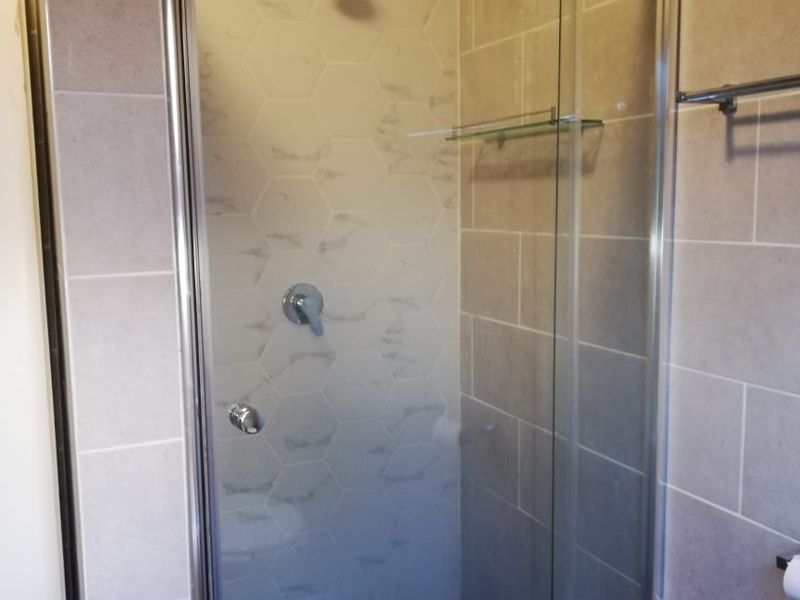A clean, modern bathroom shower featuring a glass enclosure, chrome fixtures, and neutral-toned wall tiling.
