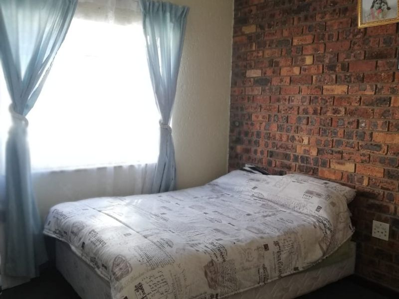 A bedroom featuring a rustic exposed brick feature wall and a window with natural light.
