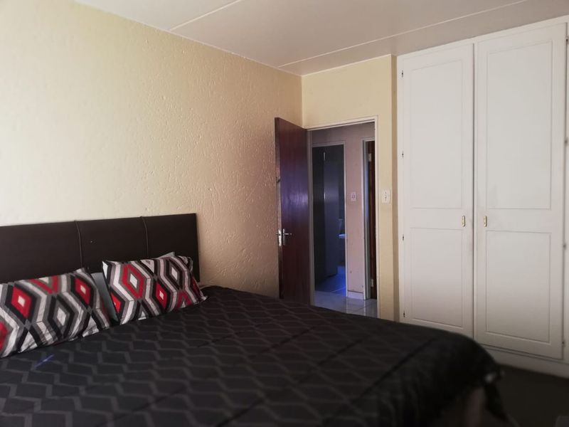 A bedroom featuring built-in cupboards and access to an adjoining room, with neutral wall finishes.