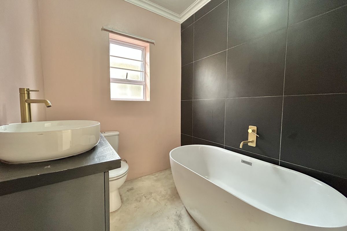 Modern bathroom featuring a freestanding bathtub, wall-mounted gold faucet, vessel sink on a vanity, and contrasting dark tiled feature wall.