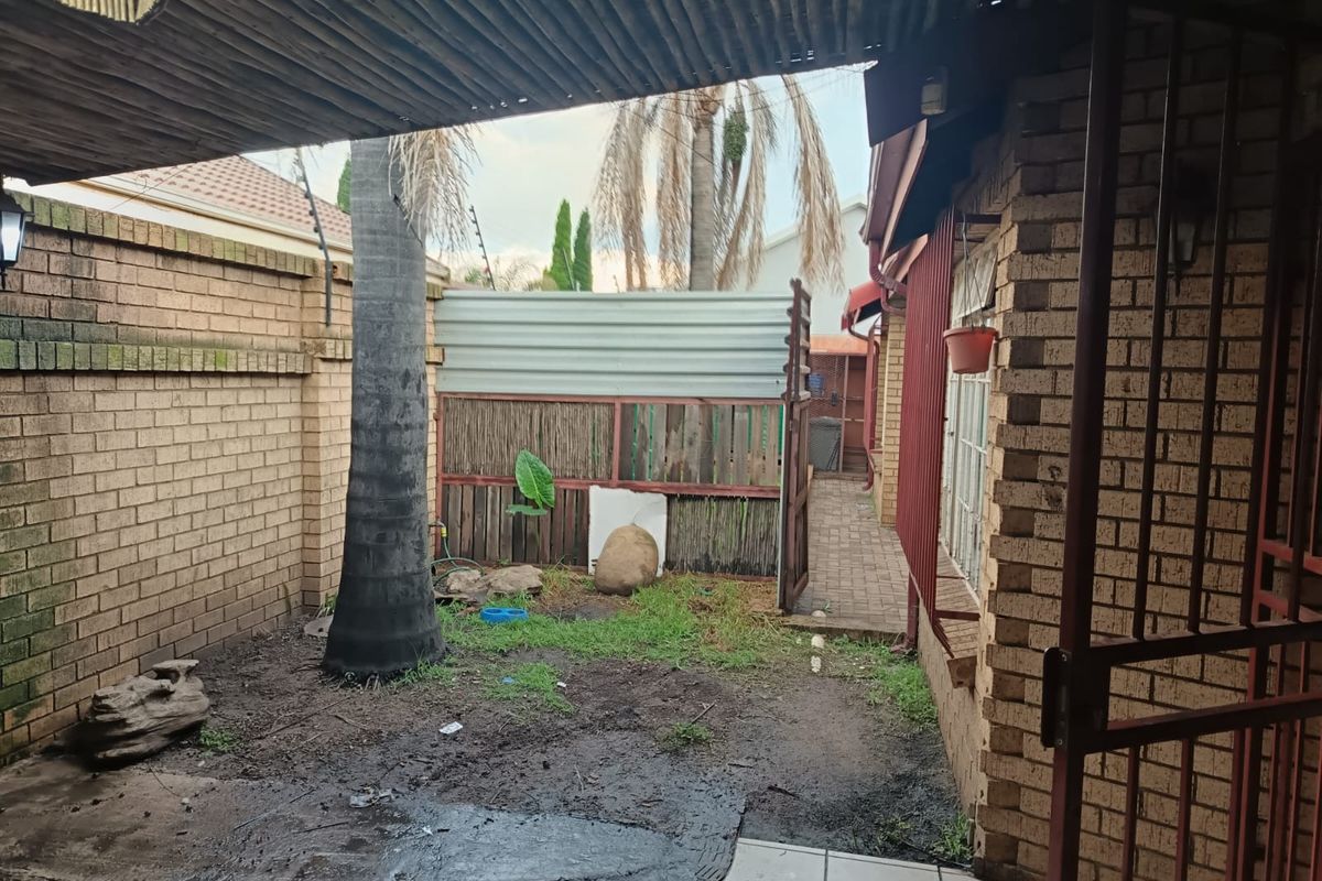 A rear courtyard area featuring brick walls, a covered patio section, and an enclosed garden space with established trees.