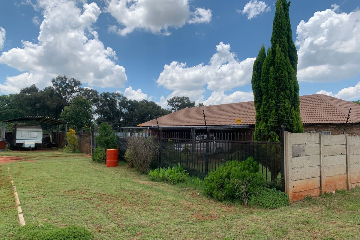 Rear exterior view of the property featuring a tiled roof, metal fencing with electric security, a carport, and a large garden area.