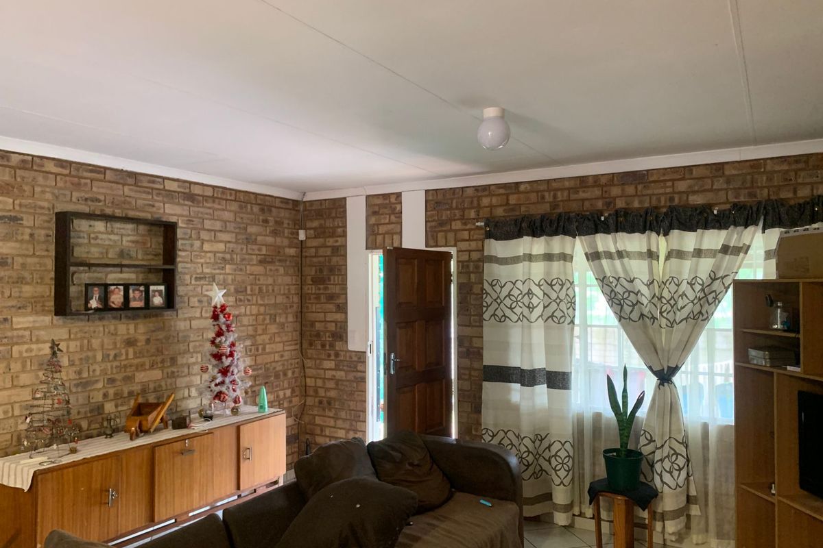 Living room featuring exposed brick walls, tiled flooring, and natural light through a window with curtains.