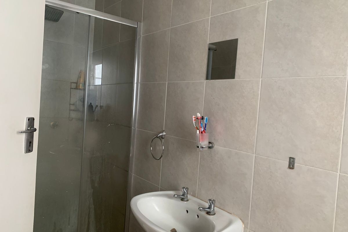 A functional bathroom featuring a shower enclosure with glass doors, a wall-mounted basin, and neutral ceramic wall tiling.