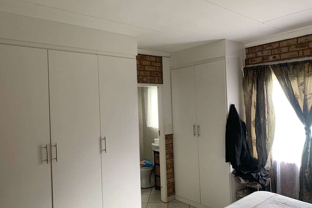 Bedroom featuring built-in cupboards, exposed brick accents, and direct access to an en-suite bathroom with tiled flooring.