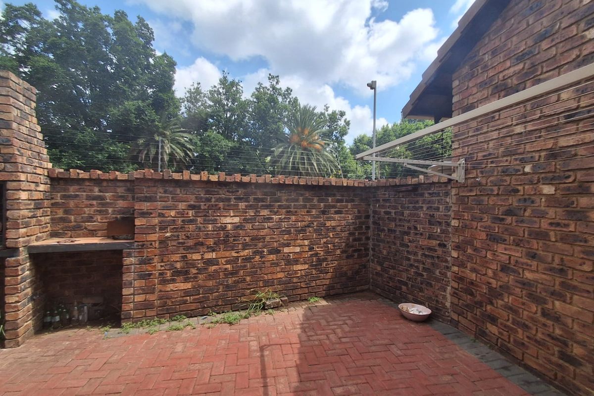A private rear courtyard featuring a built-in brick braai, red brick paving, and perimeter walling with security fencing.