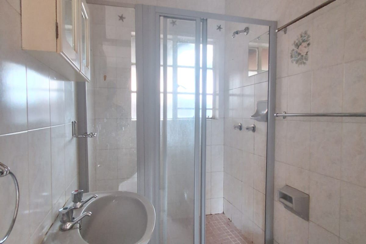 A compact bathroom featuring a pedestal basin, a shower enclosure with a glass door, and tiled walls and flooring.