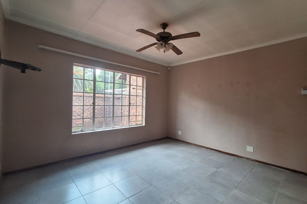 A spacious, empty living room featuring neutral tiled flooring, a ceiling fan, and a large window providing natural light.